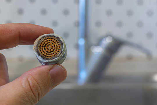 Old Tap Aerator In Hand Close Up. Kitchen Sink Faucet On The Background.