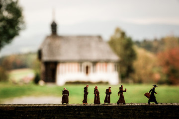 Little People: Mönche folgen dem Pfarrer vor Kapelle im Hintergrund