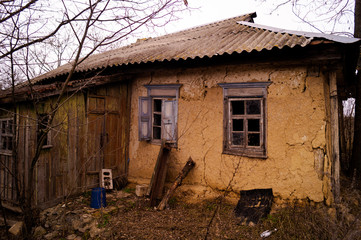 Fototapeta na wymiar Old ruined village house. Abandoned rural yard. Window frame, broken glass, peeling paint.