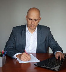 Focused man in a suit sits at a table with documents and in a computer