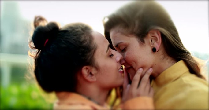 Girlfriends kissing outdoors in sunlight lens-flare. LGBT lesbian couple kiss