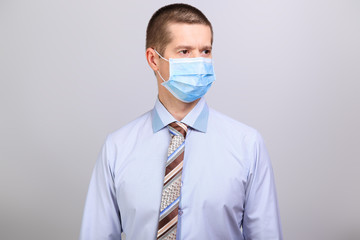 Man in light shirt, tie and medical mask looks to the right