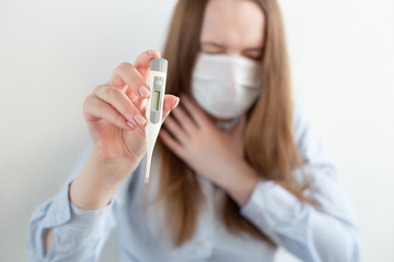 Woman in medical mask with thermometer in hand, with laptop, sitting on bed at home. Coronavirus. Business woman working from home wearing protective mask. 