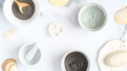 Natural organic SPA cosmetic products for face skin care. Top view clay face masks in bowls, homemade soap, sponge on marble background. Facial skin treatment concept.