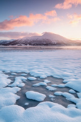 Pink early morning glow light on snow covered mountains in arctic norway, super wide panoramic scene. Scenic winter view of snowy mountain in Scandinavia. Beautiful landscape concept background.