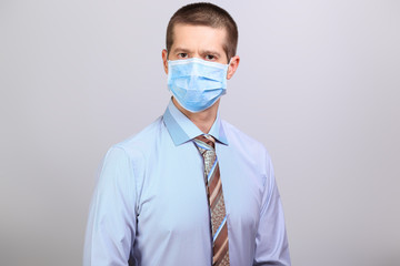 Man in light shirt, tie and medical mask looks into camera, isolated