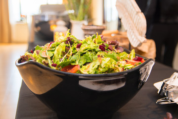 Green vegetable salad with a variety of lettuce, spinach, tomato, beetroot, arugula, nuts wth a balsamic vinegar dressing in a black bowl