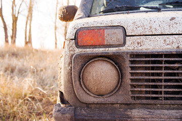 Headlight, grille and bumper of an SUV in mud closeup on the river bank - obrazy, fototapety, plakaty