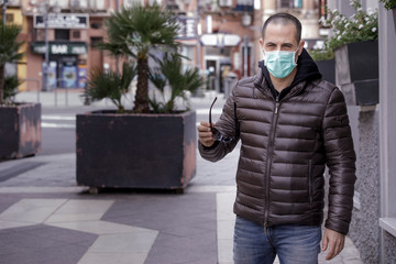 Ragazzo rasato con giubotto scuro indossa una mascherina protettiva chirurgica mentre sta in giro...