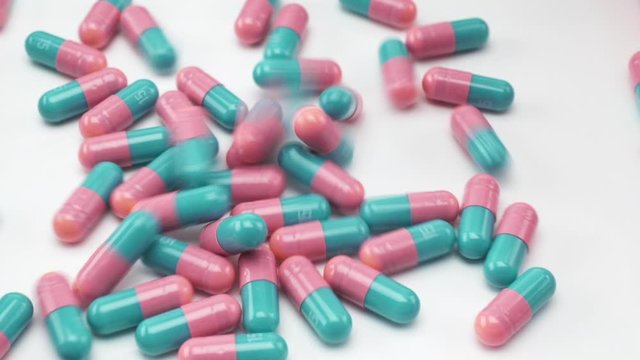 Close Up View of Blue Teal and Pink Colored Capsules Falling and Bouncing on White Background.