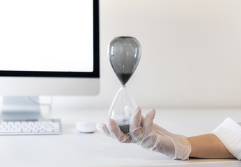 Hourglass held by a gloved hand in front of desk.