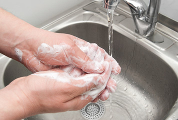 Fototapeta premium wash hands and lather fingers with foam under running water
