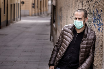 Ragazzo rasato con giubotto scuro indossa una mascherina protettiva chirurgica mentre sta in giro per la città 