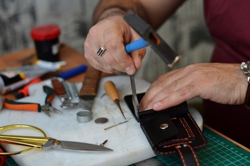 Handmade leather goods and handmade leather wallets lay on the table with crafting tools. Workflow in the workshop. Workflow in the workshop, close-up.