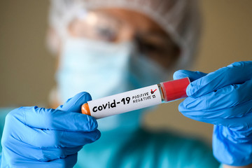 Woman in protective suit hold test tube with positive result infected with coronavirus COVID - 19. 