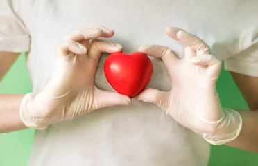 Close-up of hands in medical gloves holding red heart. Concept for charity, health insurance, love, international cardiology day, hope, donation and help during coronavirus covid-2019 pandemic