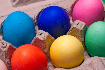 Close-up of blue, pink, red, yellow and green dyed easter eggs arranged in cardboard egg carton