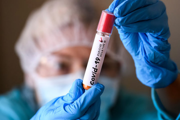 Woman in protective suit hold test tube with positive result infected with coronavirus COVID - 19.