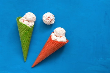 Ice cream in a red and green waffle cone on a blue background, flat lay. Top view, copy space. Summer refreshing dessert. Sundae in colored horns.