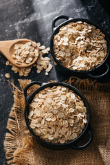 Top view of two black bowls and spoon with raw oatmeal on a black background. Breakfast with fibers...