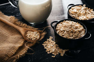 Breakfast with fibers for a balanced diet. Oat photo..Black bowl and spoon with raw oats on a black background and rustic cloth.