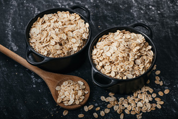 Top view of two black bowls and spoon with raw oatmeal on a black background. Breakfast with fibers for a balanced diet. Oat photo