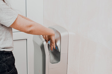 A woman in a public place dries her hands in an electric dryer. Precautions and protection for coronavirus