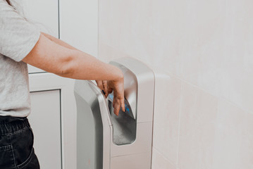 A woman in a public place dries her hands in an electric dryer. Precautions and protection for...