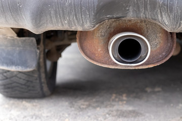 Rusty, dusty exhaust pipe of the car against a blurred background of the rear wheel. Closeup view. Selective focus