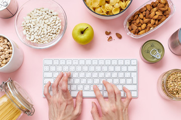 Creative layout with pantry contents and female hands typing on a keyboard. Home isolation during...