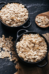 Two black bowls and spoon with raw oatmeal on a black background. Breakfast with fibers for a balanced diet. Oat photo