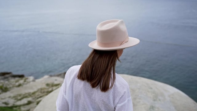 Beautiful girl in a hat stands on a cliff of the Mediterranean coast