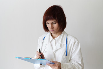 Female adult doctor stands on white background. Beautiful woman, thinking, writing