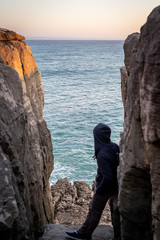 Young man leaning between two big rocks, looking to the ocean in the background.