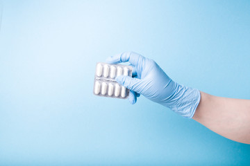 hand in a blue disposable medical glove holds a blister with white capsules blue background copy...