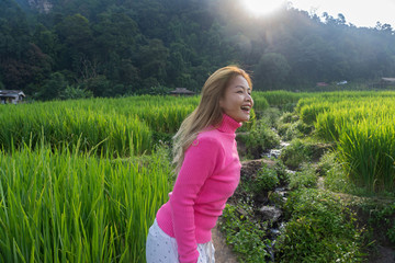 Asian woman in pink sweater smiling walking in rice field