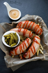 Chicken meat sausages served with ketchup, pickles and fries, vertical shot on a black stone background, selective focus