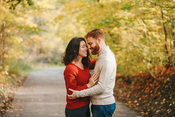 Portrait of beautiful couple man woman in love. Boyfriend and girlfriend hugging outdoor in park road path on an autumn fall day. Togetherness and happiness. Authentic real people feelings.