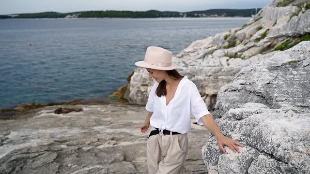 Beautiful girl in a hat stands on a cliff of the Mediterranean coast