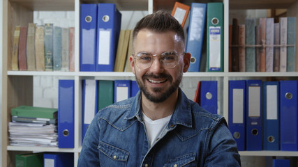 Portrait of pleased nice-looking hipster smiling cheerfully enjoying break time sitting working in modern company office. People occupation.