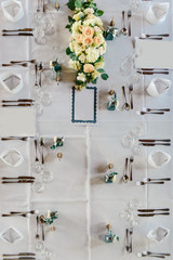 Decorated tables for guests at the wedding, there are candlestick, wine glasses, plates, napkins, tablecloth, fresh flowers