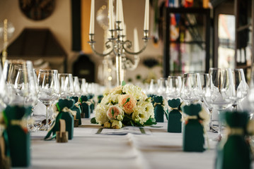 Decorated tables for guests at the wedding, there are candlestick, wine glasses, plates, napkins, tablecloth, fresh flowers