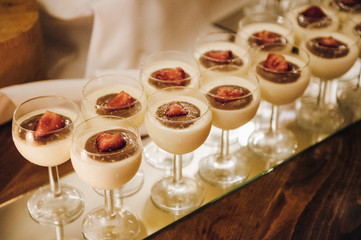 Milky desserts covered with chocolate and strawberries served in glasses are on a table