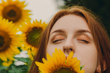 Closeup portrait of a beautiful, cute, sexy girl with red hair and sunflower flowers. Emotion of pleasure, freedom concept, lifestyle. Closed eyes.