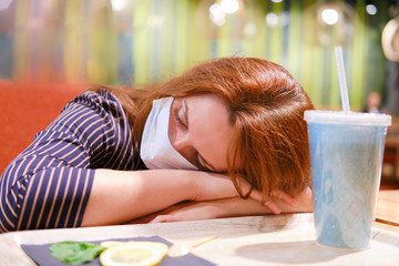 An unfortunate woman in a medical mask is lying with her head down at a table in a cafe. Trouble...