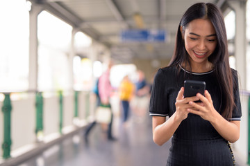 Happy young beautiful Asian tourist woman using phone on the footbridge