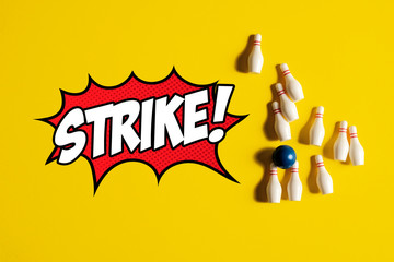 Knocked over bowling pins and bowling ball after rolling a strike on a yellow background with the word Strike written in a pop art style with bubble.