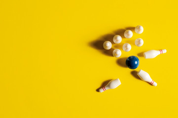 Bowling ball striking bowling pins and knocking them over on a yellow background with copy space and room for text with a right side composition.