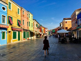 A view of the quiet town square of Burano, Italy during the early morning. A few people walk past...