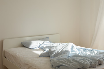 Part of the home or hotel interior, bed after sleeping in the morning  in the sun, white bed with mattress and blue linens
